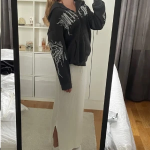 Svart hoodie med tryck - Säljer en svart hoodie med coolt vitt tryck på bröstet och ärmarna. Hoodien har dragkedja och en bekväm passform med långa ärmar och en stor huva. Perfekt för en avslappnad stil.