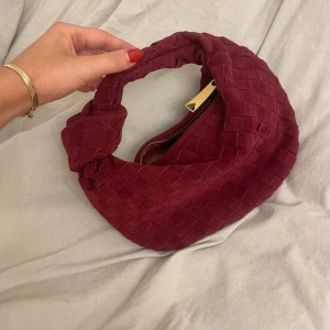 Vinröd axelväska med flätat mönster - Snygg vinröd axelväska med ett elegant flätat mönster. Väskan har en dragkedja i guld och en unik design som gör den till ett statement-piece. Perfekt för att lyfta vilken outfit som helst❤️ använd en gång! Köpt för ca 1600kr