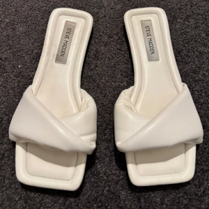 Vita sandaler från Steve Madden - Snygga vita sandaler från Steve Madden med en elegant knutdetalj på ovansidan. De har en fyrkantig tå och har en jätte skön sula, materialet är otroligt! Endast använd vid 1 tillfälle så de är precis som nya😍🤌🏼