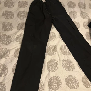 Svarta cargopants - Säljer två par svarta cargopants med flera praktiska fickor. Byxorna har en loose passform och är perfekta för en avslappnad stil. De är tillverkade i ett slitstarkt material och har en elastisk midja för extra komfort. 300kr st eller båda för 500