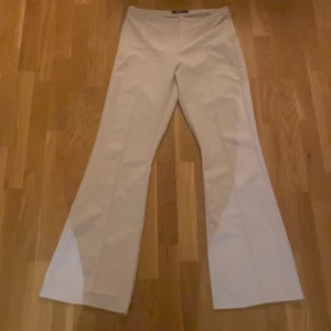 Vita byxor från Gina Tricot - Snygga vita byxor från Gina Tricot i storlek L. Byxorna har en elegant bootcut-stil och är perfekta för en stilren look. De är högmidjade och har en slät design utan synliga detaljer.