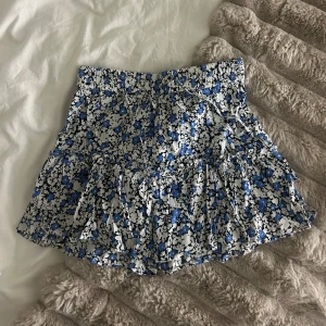 Blommig kortkjol med volang - Söt blommig kortkjol i blått och vitt med volangdetaljer. I storlek xs. Med shorts inuti 