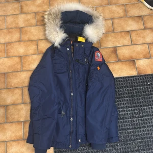 Para jumpers jacka pris kan diskuteras  - Säljer en blå Parajumpers jacka med pälsdetaljer på huvan. Jackan har flera fickor och en patch på ärmen. Perfekt för kalla dagar med sin robusta design och varma material.