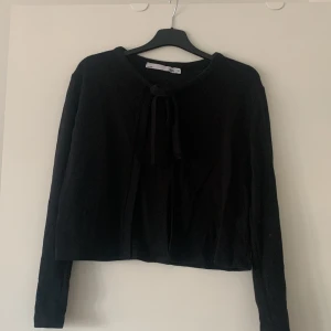 Svart kofta från 157 - Säljer en stilren svart kofta från 157 i storlek XS. Koftan har långa ärmar och en knytning framtill som ger en fin detalj. Perfekt för lager-på-lager under kyligare dagar.