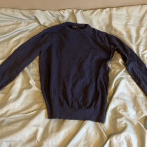 Mörkblå tröja från Henri Lloyd - Säljer en stilren cashmir mörkblå tröja från Henri Lloyd. Tröjan har en diskret broderad logga på bröstet och är tillverkad i ett mjukt material. Perfekt för en avslappnad och snygg look.