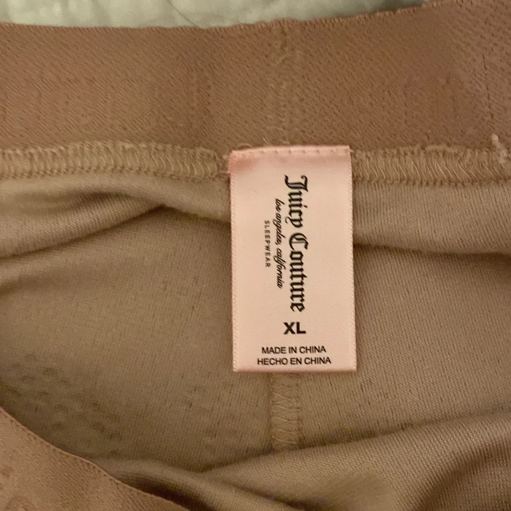 Säljer ett par snygga beige shorts från Juicy Couture i storlek XL. De är gjorda i ett mjukt material och har en elastisk midja med Juicy Couture-loggan. På baksidan finns texten 'Juicy' i glittriga stenar. Perfekta för en avslappnad dag eller en mysig hemmakväll!. Shorts.