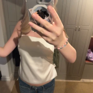 Vit  topp med knytning - Säljer en superfin vit axelbandslös topp med knytning i ryggen. Perfekt för sommardagar eller en utekväll. Toppen är i nyskick och har en stilren design som passar till det mesta. Den är gjord i ett mjukt och bekvämt material.