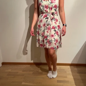 Rosablommig klänning, DryLake  - Material: 100% polyester och 100% viskos   First love belt dress  Tvättråd: 30°  Skick: Mycket bra. Axelbanden har förlängts med samma tyg, syns en liten söm, se bild