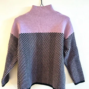 Lila och svart mönstrad stickad tröja - Säljer en snygg stickad tröja i lila och svart med ett coolt mönster. Tröjan har en halvhög krage och långa ärmar, perfekt för kyliga dagar. Den är både stilren och bekväm. Helt oanvänd. Liten i storleken. 