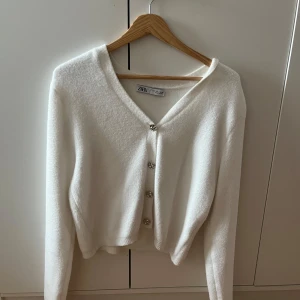Vit kofta från Zara - Säljer en stilren vit kofta från Zara med knappar framtill. Koftan har en v-ringad design och långa ärmar, perfekt för kyligare dagar. Den är mjuk och bekväm att bära. Nästan helt oanvänd, strl L men passar mig som brukar ha s. Kom privat för fler frågor!!🥰🥰