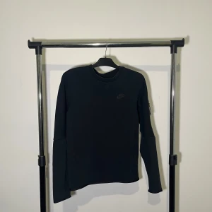Nike tech fleece crew Sweater - Säljer en stilren svart långärmad tröja från Nike. Perfekt för en sportig look eller som ett bekvämt vardagsplagg. Tröjan har en diskret Nike-logga på bröstet.