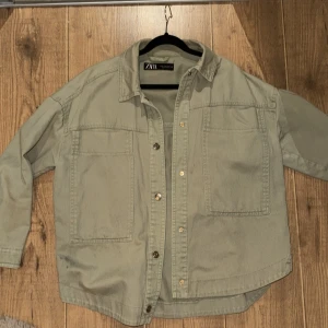 Grön jacka från Zara - Säljer en stilren beige overshirt från Zara med knappar framtill. Den har två stora bröstfickor och långa ärmar. Perfekt för lager-på-lager-stil.