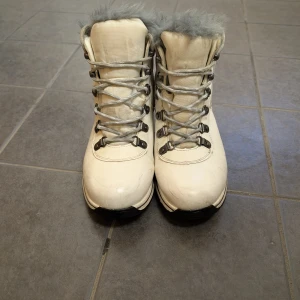 Vita vinterstövlar med grå päls - Säljer ett par vita vinterstövlar med grå pälsdetaljer och snörning. Perfekta för kalla dagar med sitt varma foder och robusta design.
