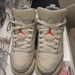 Nike Air Jordans med röda detaljer - Säljer ett par klassiska Nike Air Jordans i beige med röda detaljer. Skorna har snörning och en unik mönstrad design på sidorna. Perfekta för sneaker-entusiaster!