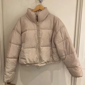 Beige pufferjacka - Säljer en snygg beige pufferjacka med dragkedja. Jackan har en hög krage och är perfekt för kyligare dagar. Den är croppad och har en modern look.