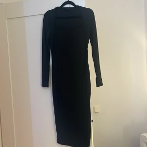 Svart långklänning - Elegant svart långklänning med långärmad design. Perfekt för en stilren look. Den har öven ett hög fin öpning vid det vänstra benet. Klänningen har en enkel och tidlös stil som passar många tillfällen.