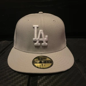 Grå keps från New Era - Sprillans ny New Era keps med broderad LA-logga framtill. Kepsen har en platt skärm och är i storlek 7 1/8, vilket motsvarar 56.8 cm.