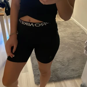 Svarta träningsshorts från Nike - Snygga svarta träningsshorts från Nike med hög midja och elastisk linning. Perfekta för gymmet eller löprundan. Diskret Nike-logga på benet.