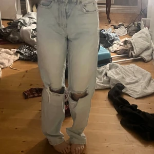 Ljusa jeans med slitningar - Säljer ett par ljusa jeans med hög midja och slitningar på knäna. De har en straight passform och klassisk femficksdesign. Perfekta för en avslappnad stil. 