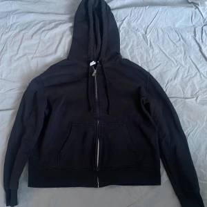 Svart hoodie från H&M Divided - Säljer en svart hoodie från H&M Divided med dragkedja och fickor framtill. Perfekt för en avslappnad stil. Den har en klassisk design med huva och långa ärmar. Väldigt bra skick.