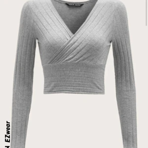 Grå ribbad omlottopp från Shein - Säljer en stilren grå ribbad omlottopp från Shein. Toppen har en v-ringad design och långa ärmar, perfekt för både vardag och fest. Den är tillverkad i ett mjukt och bekvämt material. Säljer toppen för 50kr🥰