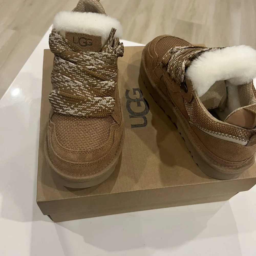 Säljer ett par snygga bruna boots från UGG med vit fuskpälsfoder. Skorna har en grov sula och snörning i ett mönstrat material. Perfekta för kyliga dagar.. Kengät.
