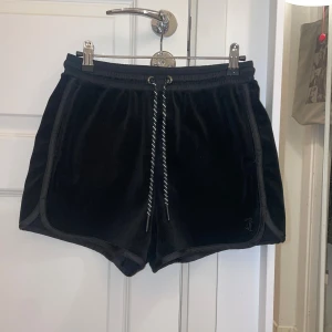 Svarta velourshorts från Juicy Couture - Snygga svarta velourshorts från Juicy Couture med broderad logga på baksidan. De har en elastisk midja med snörning för justerbar passform. Perfekta för en avslappnad och stilren look ❣️