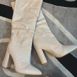 Beiga stövlar med krokodilmönster - Snygga beiga stövlar med krokodilmönster och hög klack. De har en spetsig tå och är perfekta för att ge en trendig touch till din outfit.