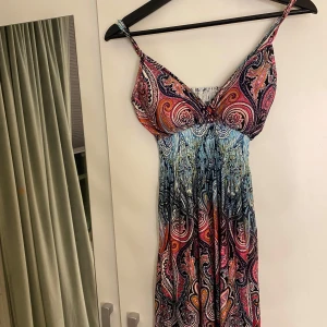 Färgglad mönstrad klänning - Säljer en färgglad klänning med ett unikt mönster. Klänningen har smala axelband och en v-ringad design. Perfekt för sommarens varma dagar. Köpt i Thailand för många år sedan, använd fåtal gånger!