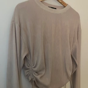 Beige ribbad tröja från Zara - Säljer en snygg beige ribbad tröja från Zara med långa ärmar och en cool snörning i sidan. Perfekt för en stilren look. Passar till många olika outfits!