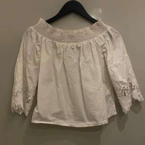 Vit offshoulder blus  - Vit offshoulder blus från New Look. Blusen har en elastisk smock vid halsen/axlarna och lite vida trekvartsärmar med grov spets/broderade blommor längst ut.