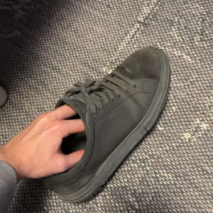 Svarta sneakers från Axel Arigato - Snygga svarta sneakers från Axel Arigato med stilren design. Skorna har snörning och en diskret logga på sidan. Perfekta för en casual look.