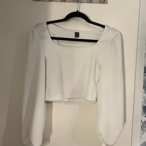 Vit croppad topp - Snygg vit croppad topp med långa vida ärmar och en fyrkantig halsringning. Perfekt för en stilren look. Väldigt stretchig i material. 