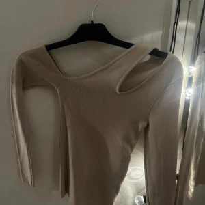 Beige oneshoulder topp - Snygg beige oneshoulder topp med lång ärm. Perfekt för en stilren look med en unik twist. Vet inte var den är ifrån då den är köpt utomlands. Aldrig använd. Skicka för frågor😊
