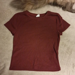 Vinröd ribbad topp från Gina Tricot - Säljer en vinröd ribbad topp från Gina Tricot i storlek S. Toppen har korta ärmar och en rund halsringning, perfekt för en avslappnad stil.
