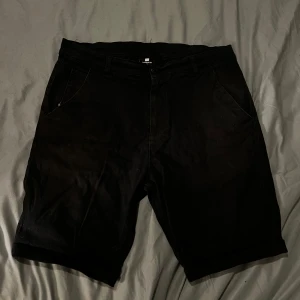 Svarta shorts från Sweet Skibs - Snygga svarta shorts från Sweet Skibs i storlek w33. De har en klassisk design med dragkedja och knappar. Perfekta för en stilren look. Chinos aktiga