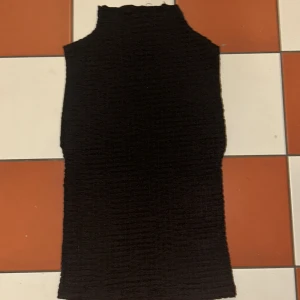 Svart ärmlös topp från Zara - Snygg svart ärmlös topp från Zara i ett ribbat material. Perfekt för lager-på-lager eller att bära som den är. Toppen har en hög hals och en stilren design.