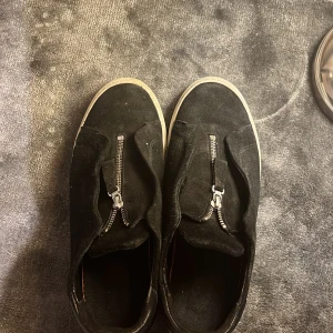 Savrta arigatos med dragkedja - Snygga svarta arigatos i mocka med dragkedja . dessa skor kombinerar stil och komfort perfekt. Använder inte dom längre har andra  ni får box och påse till den ochså