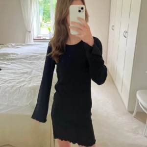 Svart klänning med lång ärm - Snygg svart klänning med lång ärm och ribbad struktur. Perfekt för en stilren look. Klänningen har en tight passform och är knälång.