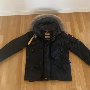 Svart vinterjacka från Parajumpers - Säljer en svart Parajumpers vinterjacka i storlek small. Jackan har en avtagbar pälsfodrad huva och flera praktiska fickor. Den är perfekt för kalla vinterdagar och har snygga detaljer som en gul rem och en PJS-logga på ärmen. Dragkedja och knappar framtill för extra värme.🖤obs ‼️ endast frakt. Frakt PostNord 