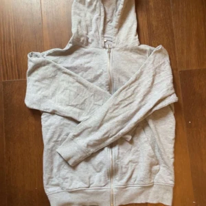 Ljusgrå hoodie - En ljusgrå hoodie med dragkedja i storlek 159/164