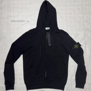 Stone Island Hoodie - Svart Stone Island Hoodie, zip-up, helt ny och oanvänd. Trendig och stilren design. Perfekt för alla tillfällen. Säljes billigt! Kontakta mig vid intresse.