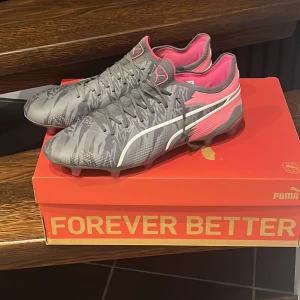 Fotbollskor Puma King Ultimate FG/AG - Storlek 42,5 Grå/rosa Puma King fotbollskor. Nypris 2400 kr. Skick 9/10. Andvända cirka 10 fotbollstränningar. Några funderingar så Äre bara att kontakta. Villig för prisförslag.
