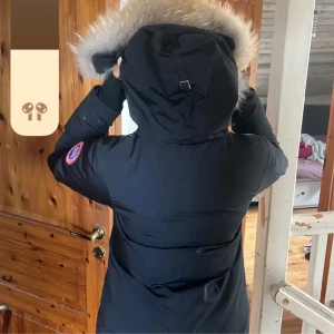 2000 vid snabb äffär!! - Säljer en svart dunjacka från Canada Goose med en mysig pälsfodrad huva. Jackan är perfekt för kalla vinterdagar och har en snygg passform. Den har långa ärmar och en dragkedja framtill. Märkesloggan syns tydligt på ärmen.