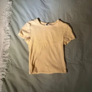 Beige kortärmad topp - Säljer en enkel och stilren beige mag tröja med korta ärmar. Perfekt för vardagsbruk eller att styla upp med accessoarer. Toppen är i ett mjukt och bekvämt material.