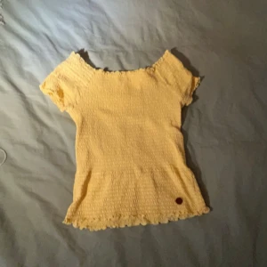 Gul ribbad topp - Säljer en söt gul ribbad topp med korta ärmar. Den har en fin volangdetalj vid ärmslut och nederkant, vilket ger den en extra touch. Man blir lite varm i den men älskar den så himla mycket. Men säljer den pga den är för liten💗