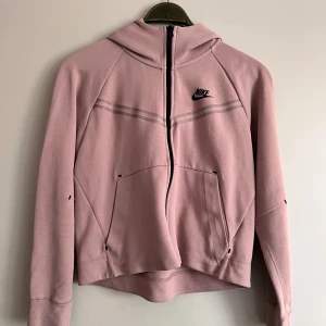 Rosa hoodie från Nike - Säljer en superfin  hoodie från Nike. Den har en dragkedja framtill och en snygg svart Nike-logga på bröstet. Hoodien är långärmad och har en skön passform. Perfekt för både träning och vardag! Super bra skick, enda defekten är en fläck runt loggan som inte syns så mycket men värt att nämna. Använd 1 gång, inga defekter utöver det nämnda.  Pris kan diskuteras  Köpt för 1449kr