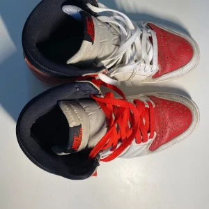 Nike Air Jordans i rött och vitt - Säljer ett par klassiska Nike Air Jordans i rött och vitt. Skorna har en snygg design med det ikoniska Air Jordan-logotypen på sidan. De är tillverkade i skinn och har röda snören som matchar de röda detaljerna. Perfekta för både vardag och fest!