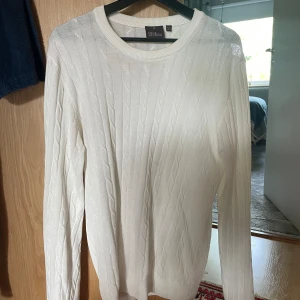 Kabelstickad Oscar Jacobson tröja - Säljer denna vita stilrena stickade tröjan som är använd ett fåtal gånger och kommer där med ett fint skick. Tröjan är lite missfärgad på kragen men är inget som syns. Nypris: 1500kr Mitt pris: 400kr. Priset är diskuterbart! DM:a vid intresse. 