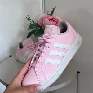 Rosa sneakers från Adidas - Säljer ett par snygga rosa sneakers från Adidas. De har de klassiska tre vita ränderna på sidan och en vit sula. Skorna är i syntetmaterial och har snörning framtill. Perfekta för vår och sommar!